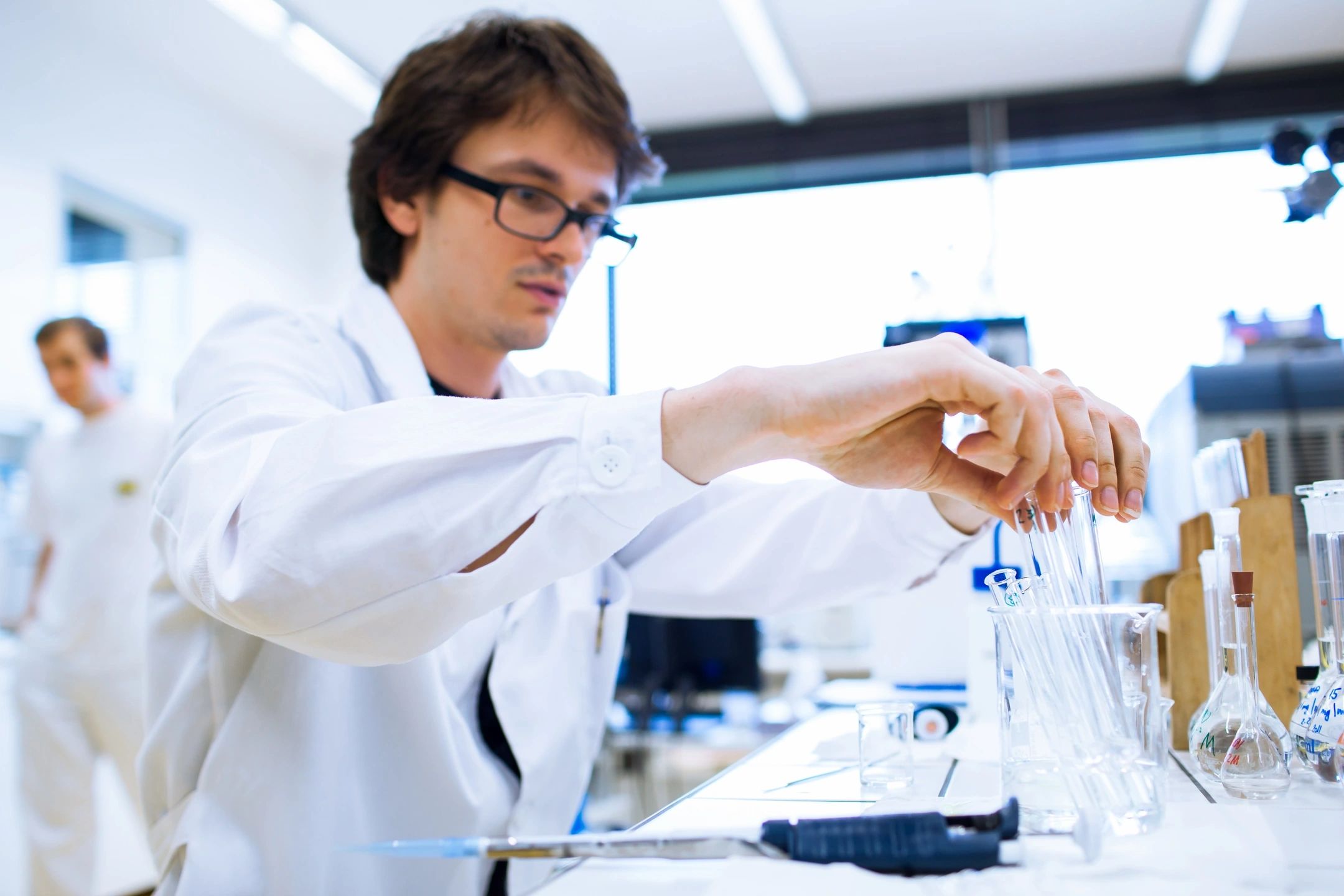 Man in white lab coat grabbing glass tubes